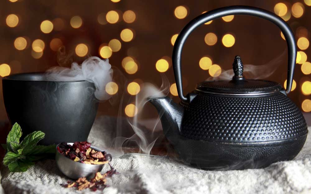 Black tea cup and tea pot sitting on white table with epice tea leaves in front