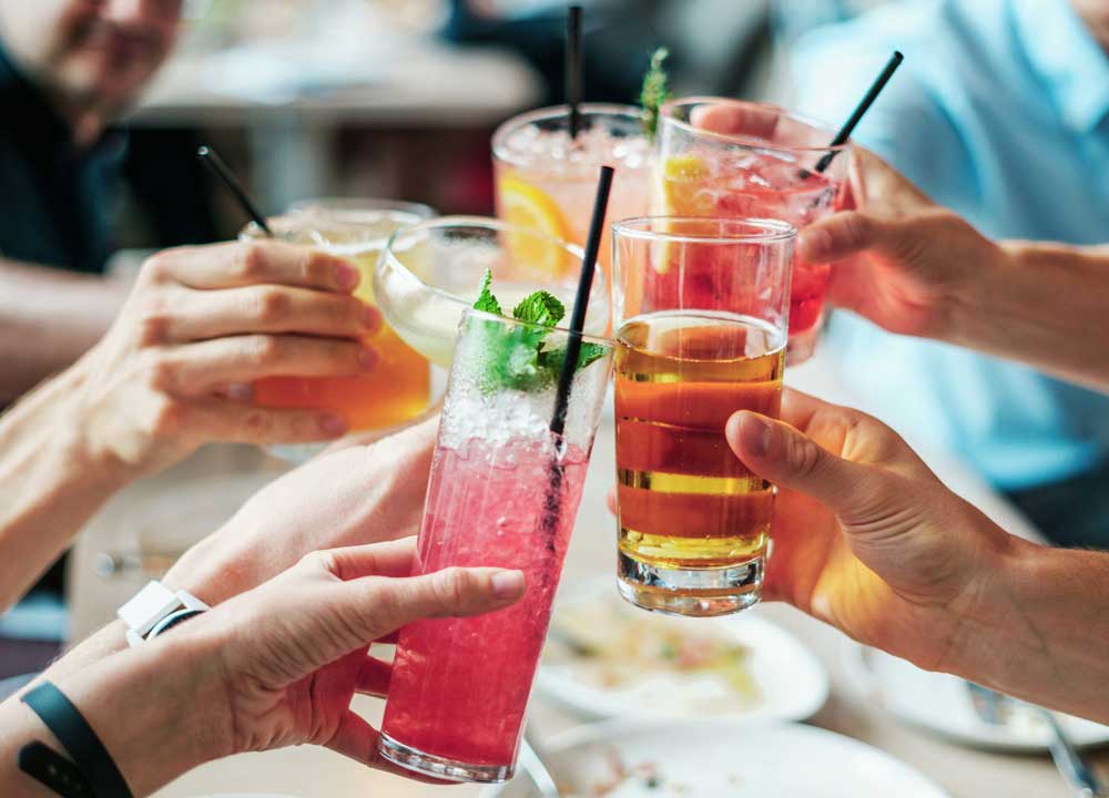 People holding glasses of colourful cocktails with black straws