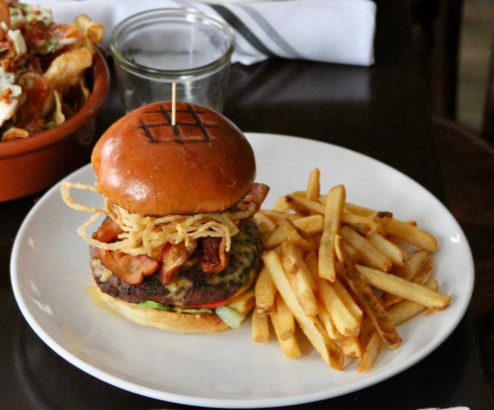 Burger and fries on a white plate with nachos in a red bowl beside it.